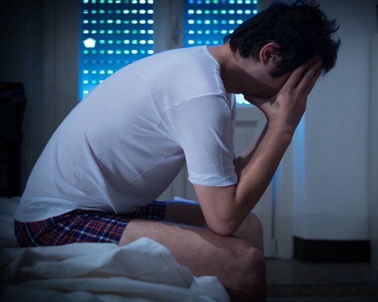 Man sitting on the edge of bed in nightwear resting his face in both hands